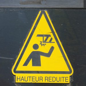 A yellow triangle sign demonstrates a head potentially hitting a low beam. The text is in a language other than English.