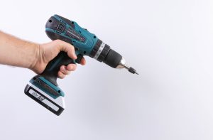 A hand is holding a hand drill with their finger on the trigger (a dead man switch).