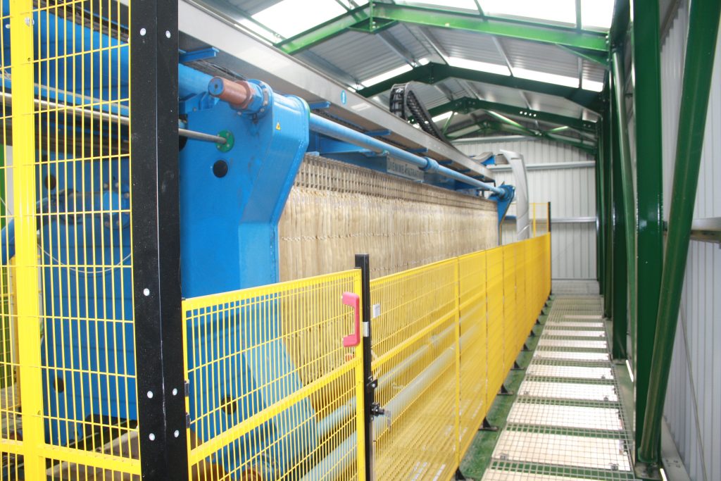 A large machine has bright yellow safety fencing around its moving parts.