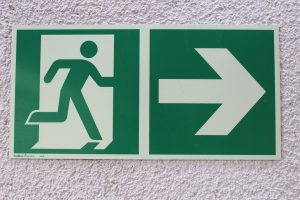 A green sign depicts a person moving through an open door with an arrow indicating where the closest building exit is located.