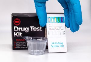 A hand in a blue medical glove displays the components of a drug test kit including a box with the words drug test kit.