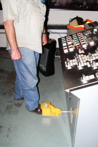 A man is standing in a train driver's cabin with his shoe tapping a dead man's switch which enables the train controls to work.