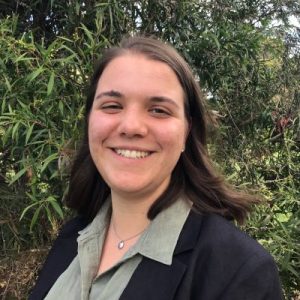 Image of a female in her 20's with brown hair, wearing a green shirt and black blazer.