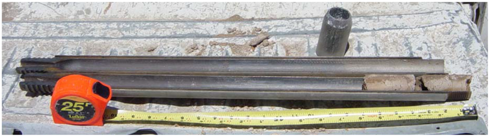 A barrel split into two horizontal halves, the half closer to the camera showing a sample core at the end. The barrel lies next to a tape measure.