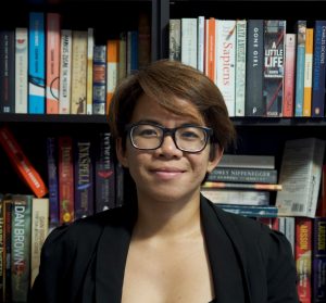 A photo of the author, Klaire Somoray standing in front of their books.