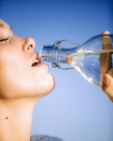Woman drinking water from glass bottle against a blue sky