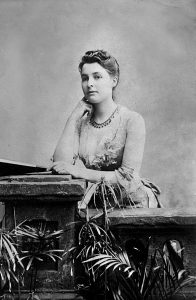 White woman in a seated pose. she is neatly dressed and wear a necklace
