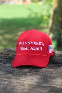 A red baseball cap with 'make america great again' on the front and an American flag on the side