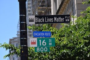 The street sign for the Black Lives Matter Plaza is white text on black, differing from other street signs that are white text on green or blue.