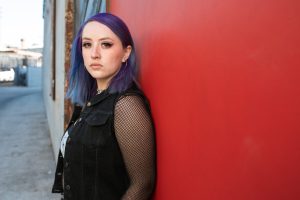 Woman with purple hair standing in front of a red wall.