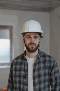 A smiling man in a checked shirt and wearing a hard hat.