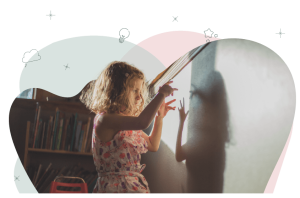 A child is standing in front of a blackboard making shadow finger puppets.