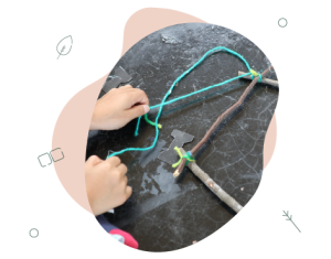 A child's hands tying some sticks together with blue coloured wool