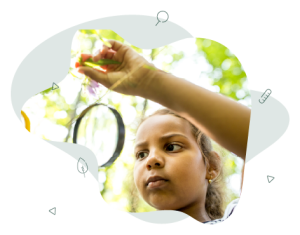 A child is standing in a garden holding a magnifying glass and investigating at a leaf.