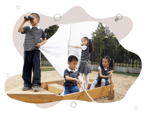 Four children in school uniform pretend playing in a wooden boat that is in the middle of a large sandpit