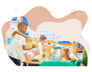 Group of children gathered around a school room table. The children are playing a game with large yellow dice and large egg timers.