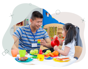 A smiling male teacher and student playing with plastic teacups and food in the classroom