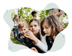 A class of children is in a green house. Three children are focusing on some moss growing on a stump