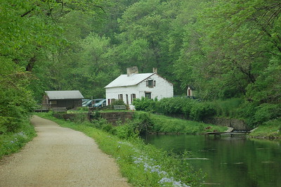 Photograph of a white house next to a canal with a road and surrounding greenery