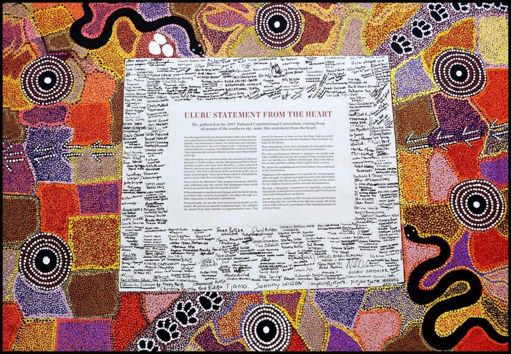 Photograph of the Uluru Statement from the Heart. A colourful dot painting artwork surrounds the statement along with over 250 delegates who attended the conference and reached consensus.