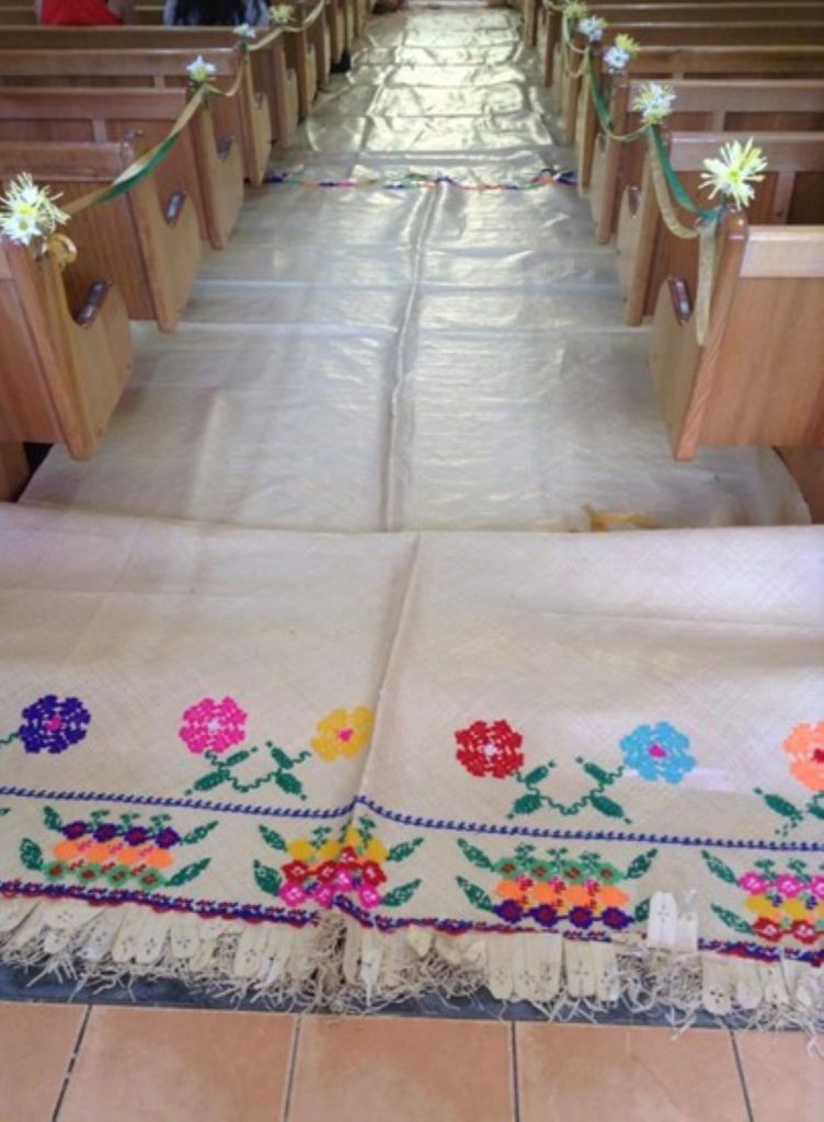 The interior of a church with wooden pews lining a central aisle covered by a white mat runner.