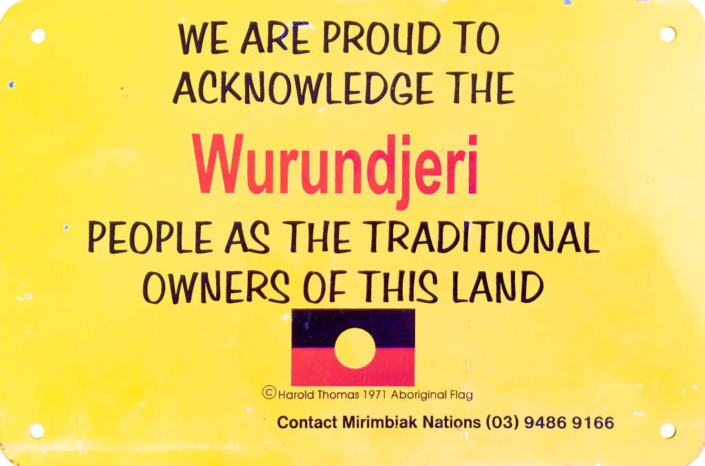 Yellow sign acknowledging Wurundjeri people as traditional landowners, featuring Aboriginal flag by Harold Thomas and contact info for Mirimbak Nations.