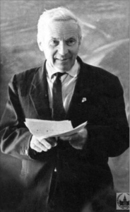 Black and white photograph of Andrey Komogorov standing in front of a chalkboard, holding pages of notes.