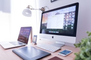 A large desktop Apple Mac computer with an Apple laptop and Iphone on a desk.