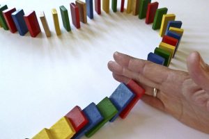 A line of brightly coloured wooden dominos is blocked by a hand entering the picture.
