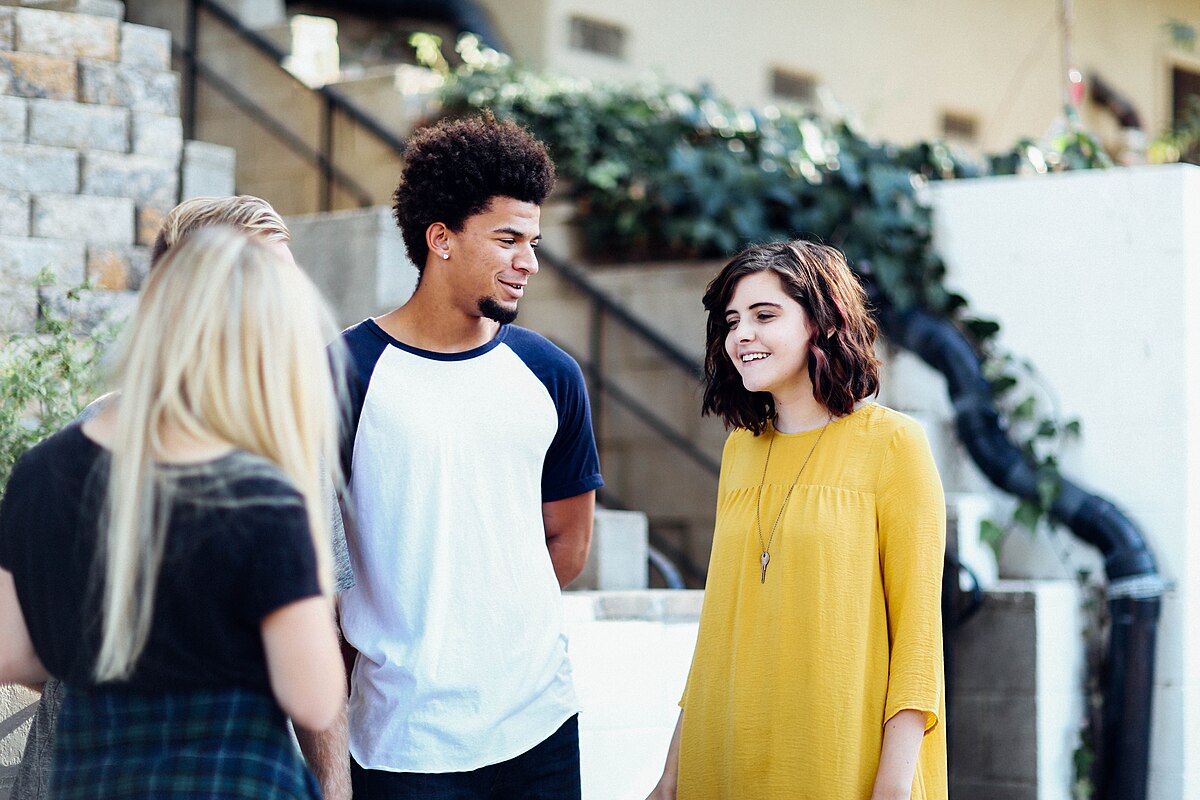 Two women and a man engaged in conversation outside a building, standing in an urban setting with a modern architectural backdrop