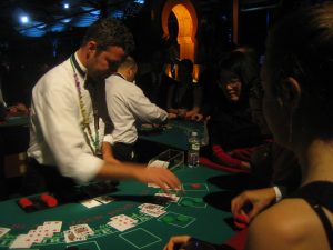 A white male standing behind a Blackjack table and dealing cards to three women in a casino. The women are putting chips down at the Blackjack table.