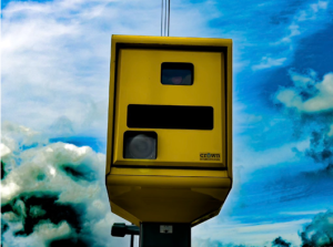 A bright yellow box containing a speed camera. There are three black squares on the box, indiciating the different cameras and other electronic gear in use.