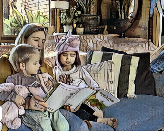 A woman sitting on the couch with two children. The smaller child is in the mother’s lap the older child is sitting next to the mother. They are all looking at a book that the mother is holding.