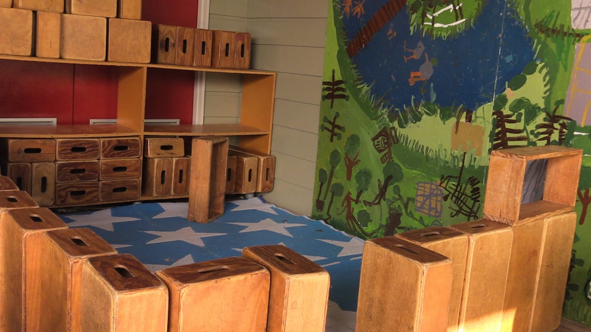 In a classroom the are large wooden blocks stacked together to create a wall with a gateway.