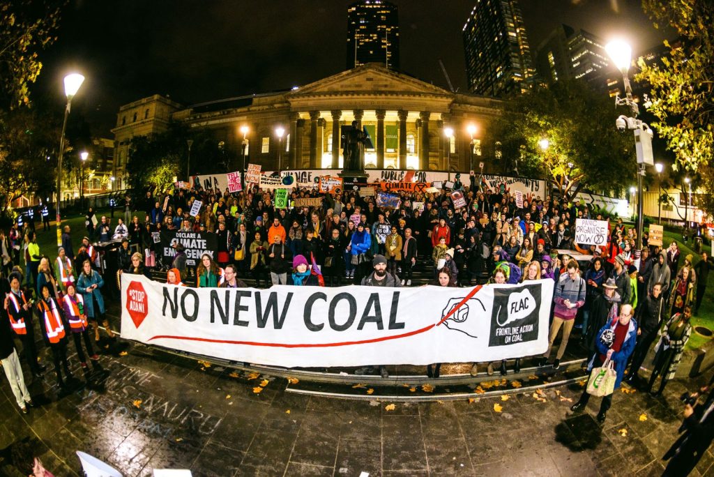 Fisheye photograph at night that depicts a group of protesters at the front of State Library Victoria holding a large banner that reads " No New Coal".